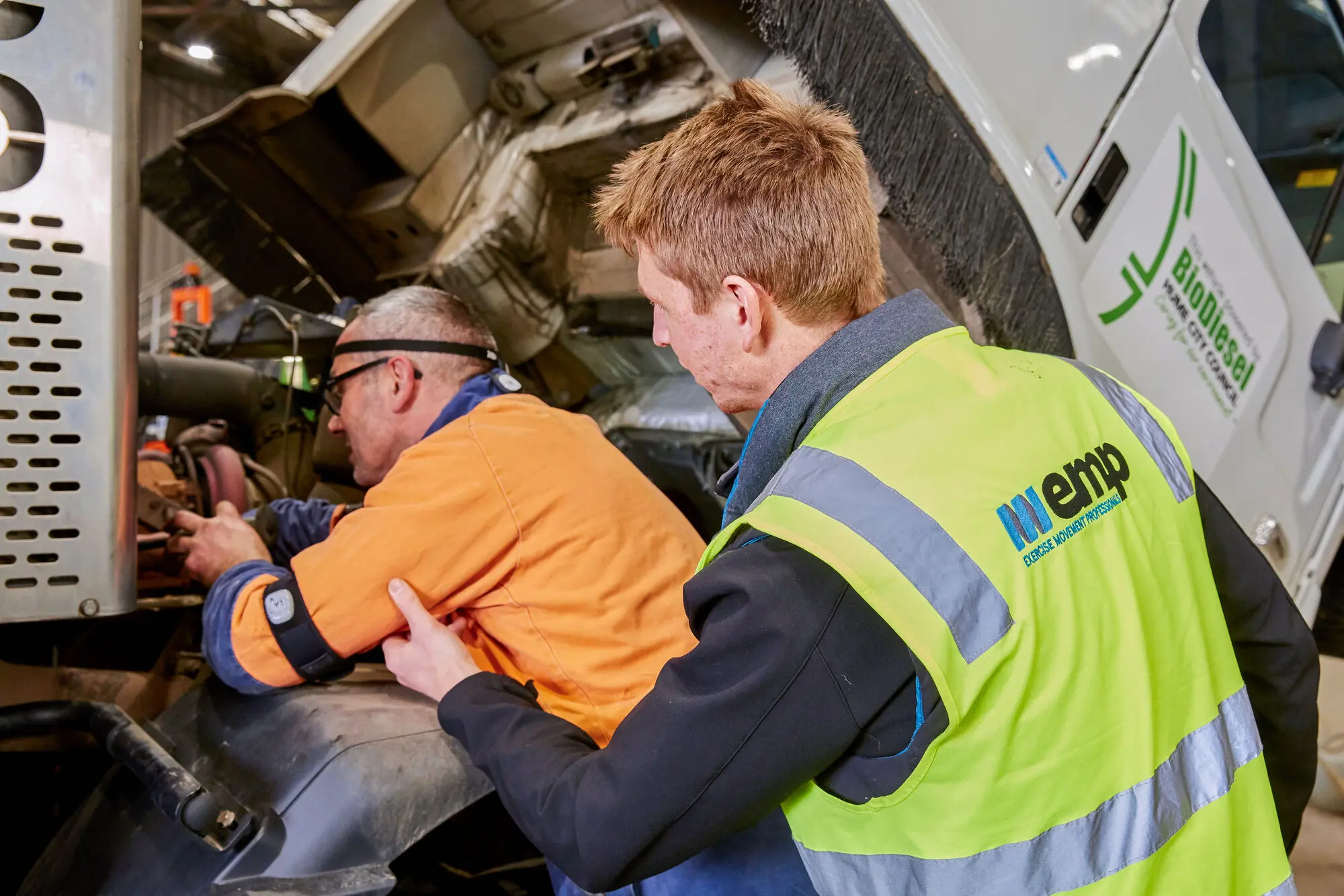 An EMP Onsite clinician fitting a wearable motion sensor to a mechanic working inside a truck engine bay.