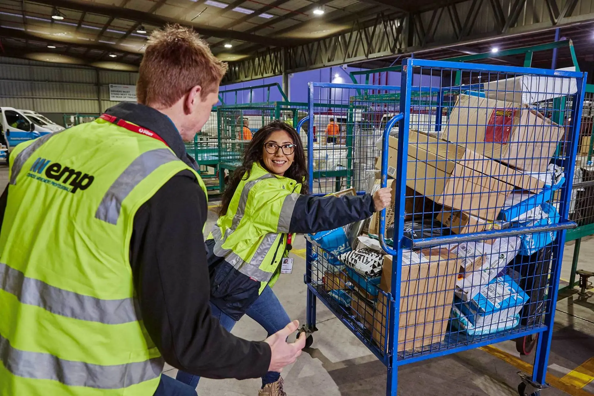 An EMP Onsite clinician coaching a warehouse worker on safe handling beside parcel cages.
