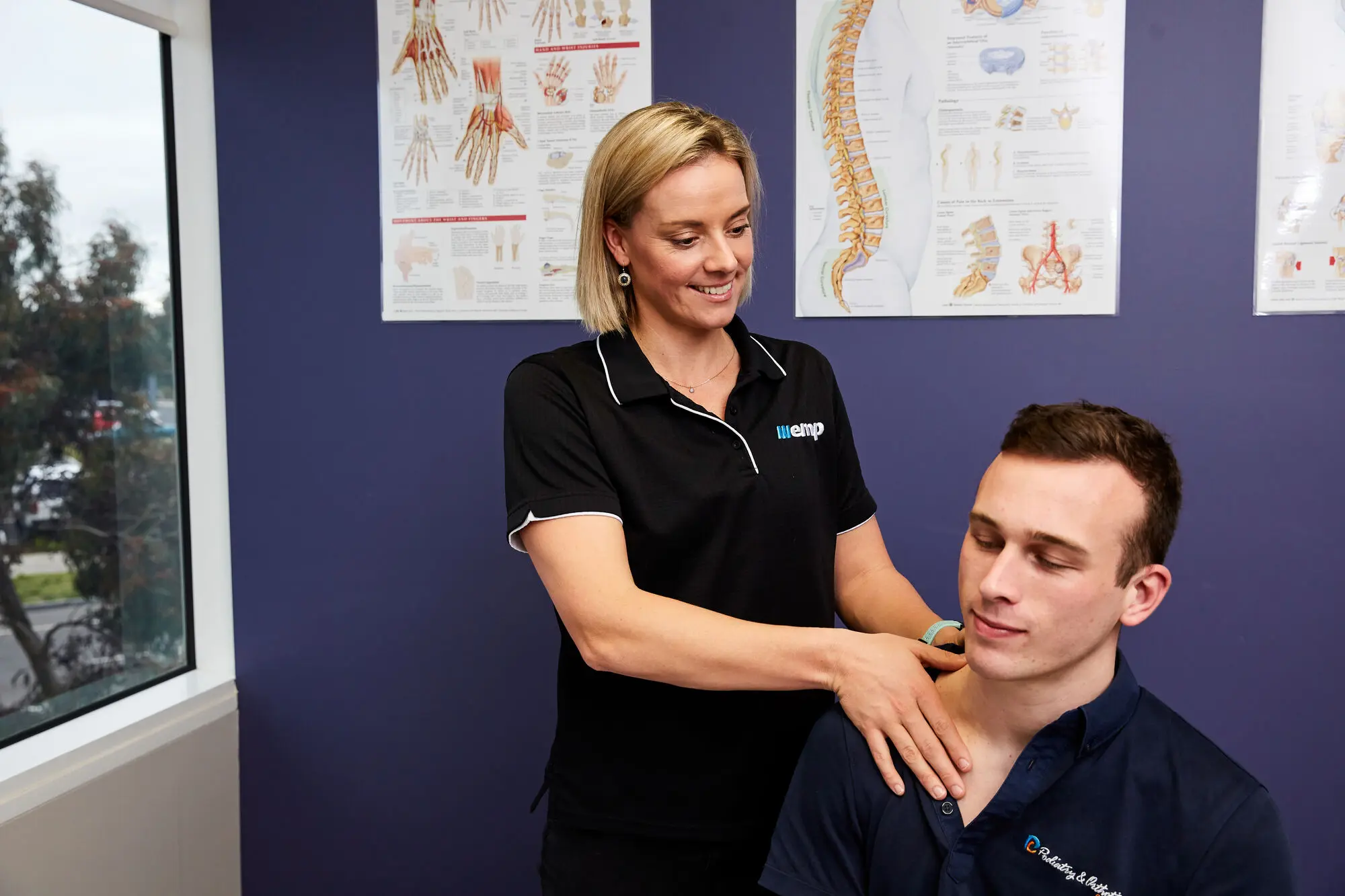 An EMP Onsite physiotherapist assessing a patient's shoulder in a treatment room.
