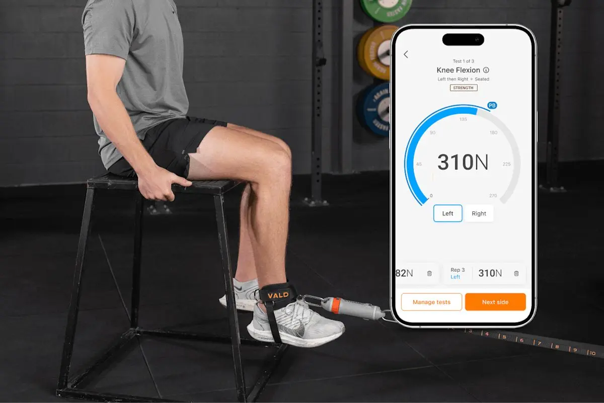 A worker doing a seated knee strength test with VALD DynaMo, with results on a phone